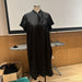 A black short-sleeve dress displayed on a mannequin torso or a Dress Form. The dress has a high collar with tie details at the front and side.